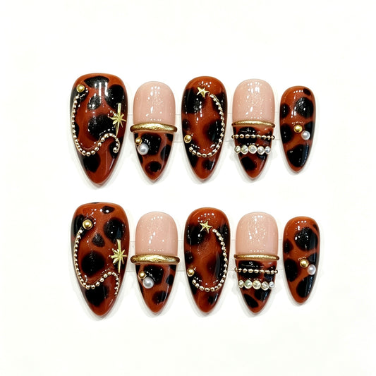Amber tortoiseshell press-on nails with gold stars, pearl chains and black accents